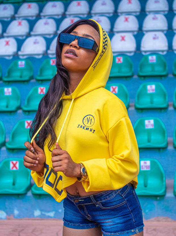 Person wearing a yellow hoodie with a logo in an outdoor setting with green and blue seats.